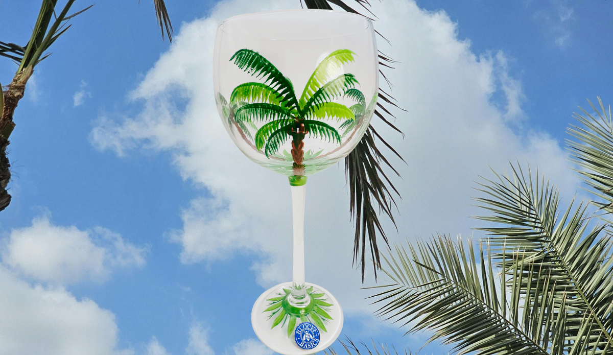 Block Basics Palm Breeze hand painted wine glass displayed beneath tropical palm trees