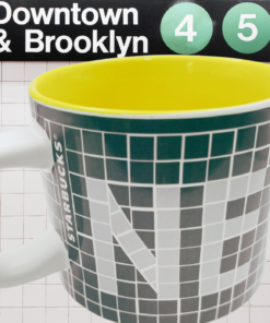 Starbucks New York Subway Mug displayed beneath a Downtown and Brooklyn subway sign with yellow interior visible