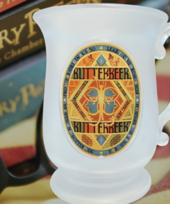 Harry Potter Pedestal Butterbeer Souvenir Mug displayed with Harry Potter books, reading glasses, and a cozy blanket