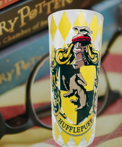 Harry Potter Hufflepuff House Crest Glass displayed with Harry Potter books, reading glasses, and a striped blanket