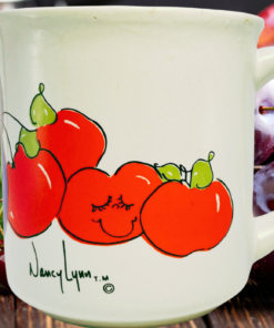 Nancy Lynn Plums and Cherries Mug displayed with ripe purple plums, red cherries, green leaves, and smiling fruit artwork.