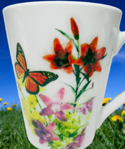 Monarch butterfly floral bone china mug displayed in sunny yellow wildflower meadow