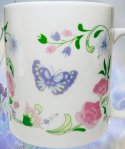 Pastel butterfly floral mug displayed in a soft purple and blue wildflower garden scene