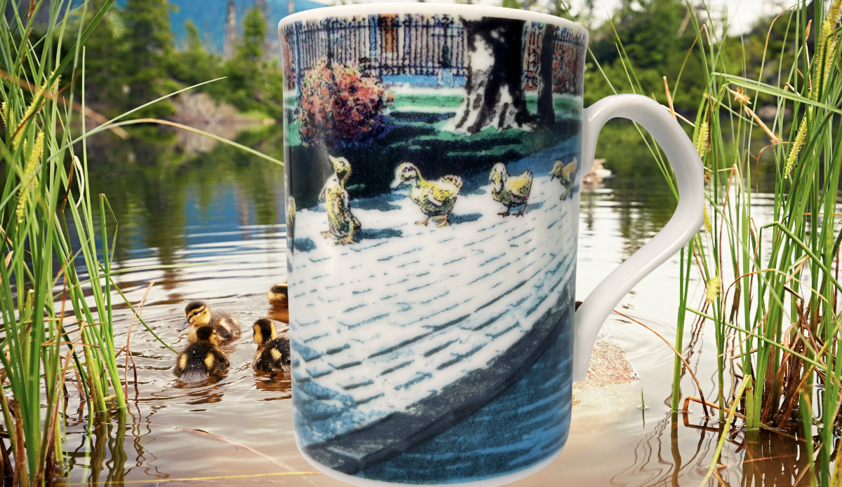 Ducklings II Mug displayed beside a peaceful pond with ducklings swimming among green reeds and natural scenery.