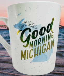 Good Morning Michigan Coffee Mug displayed beside blue water and a Michigan bridge at sunset