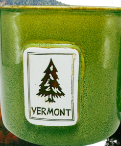 Vermont Pine Tree Souvenir Mug displayed beside an autumn lake surrounded by colorful Vermont foliage