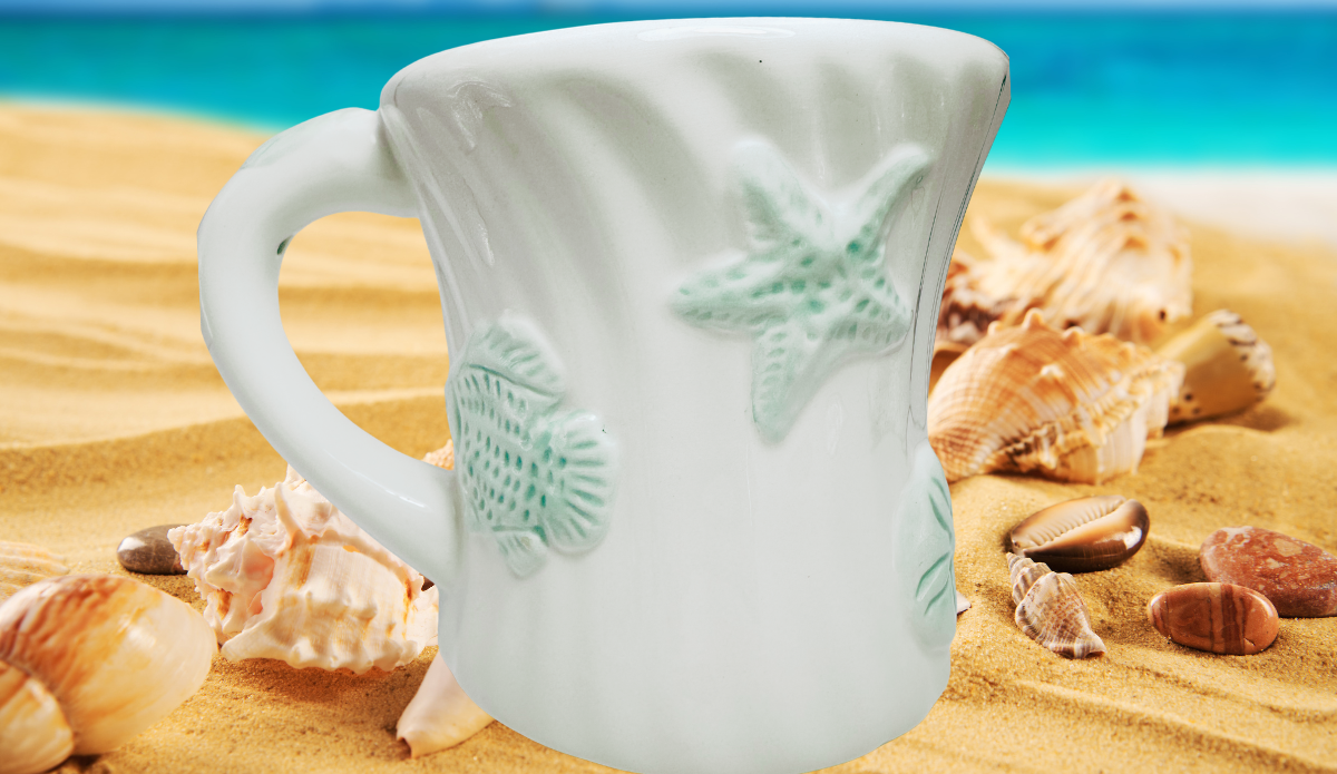 Seafoam Green Seashell Mug displayed on sandy beach with seashells and turquoise water