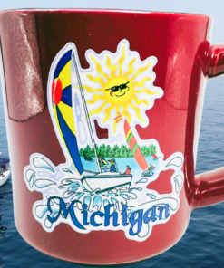Michigan Sailboat Souvenir Coffee Mug displayed against blue lake water with sailboats