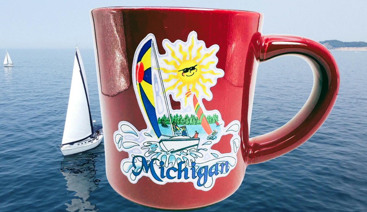 Michigan Sailboat Souvenir Coffee Mug displayed against blue lake water with sailboats