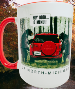 Up North Michigan Black Bear Funny Coffee Mug displayed against colorful autumn woods beside water