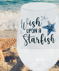 Starfish Acrylic Wine Glass displayed on sandy beach beside a starfish and ocean waves