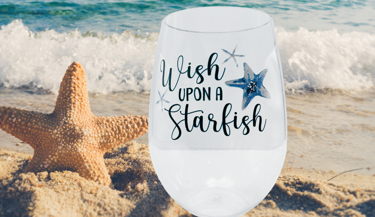 Starfish Acrylic Wine Glass displayed on sandy beach beside a starfish and ocean waves