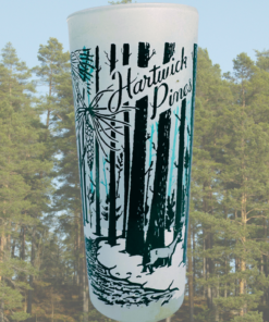 Vintage Hartwick Pines Michigan souvenir glass displayed against a pine forest setting