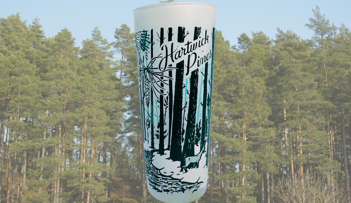 Vintage Hartwick Pines Michigan souvenir glass displayed against a pine forest setting