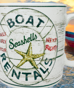 Casa Moda Boat Rentals Seashells Mug displayed beside ocean water, sunset sky, and small boat