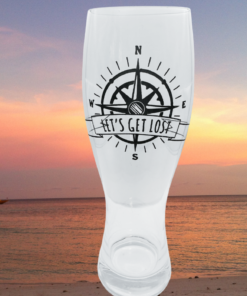 Compass Pilsner Glass displayed against beach sunset with ocean water and boats