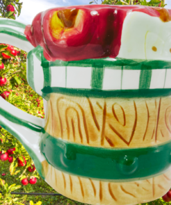 3D Apple Basket Ceramic Coffee Mug displayed in a sunny apple orchard filled with red apples and green foliage