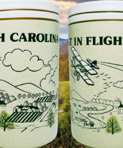 North Carolina First in Flight Souvenir Mug lifestyle scene against autumn mountains golden foliage and green meadow