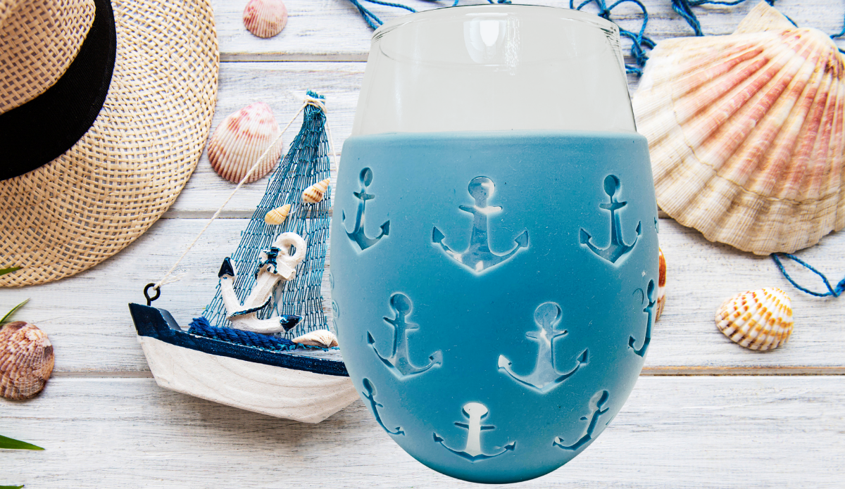 Blue Anchor Stemless Wine Glass with seashells, straw hat, sailboat, and coastal tabletop setting