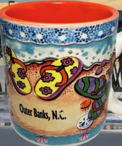 Outer Banks Flip Flops Souvenir Mug displayed in the Outer Banks with ocean pier beach waves and coastal sky
