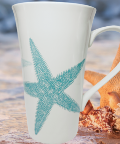 222 Fifth Starfish Mug displayed on beach with starfish coral seashells and ocean water