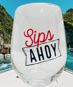 Sips Ahoy Stemless Wine Glass displayed on boat with turquoise water and coastal cliffs