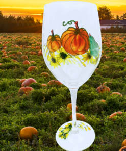 Hand Painted Pumpkins Wine Glass displayed in a pumpkin field at sunset with orange pumpkins and autumn scenery