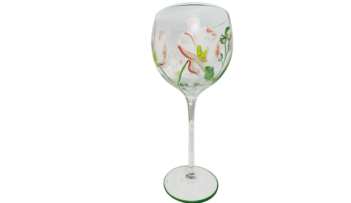 Middle view of peach pink hand painted balloon wine glass featuring unopened flower buds, curved green stems, pointed leaves, and pale coral blossoms.
