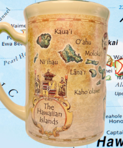 Island Heritage Hawaii Map Mug photographed against a colorful geographical map of Hawaii with blue Pacific Ocean background.