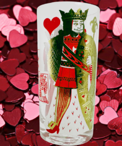 King of Hearts Playing Card Highball Glass displayed against scattered red, burgundy, and pink heart-shaped decorations.