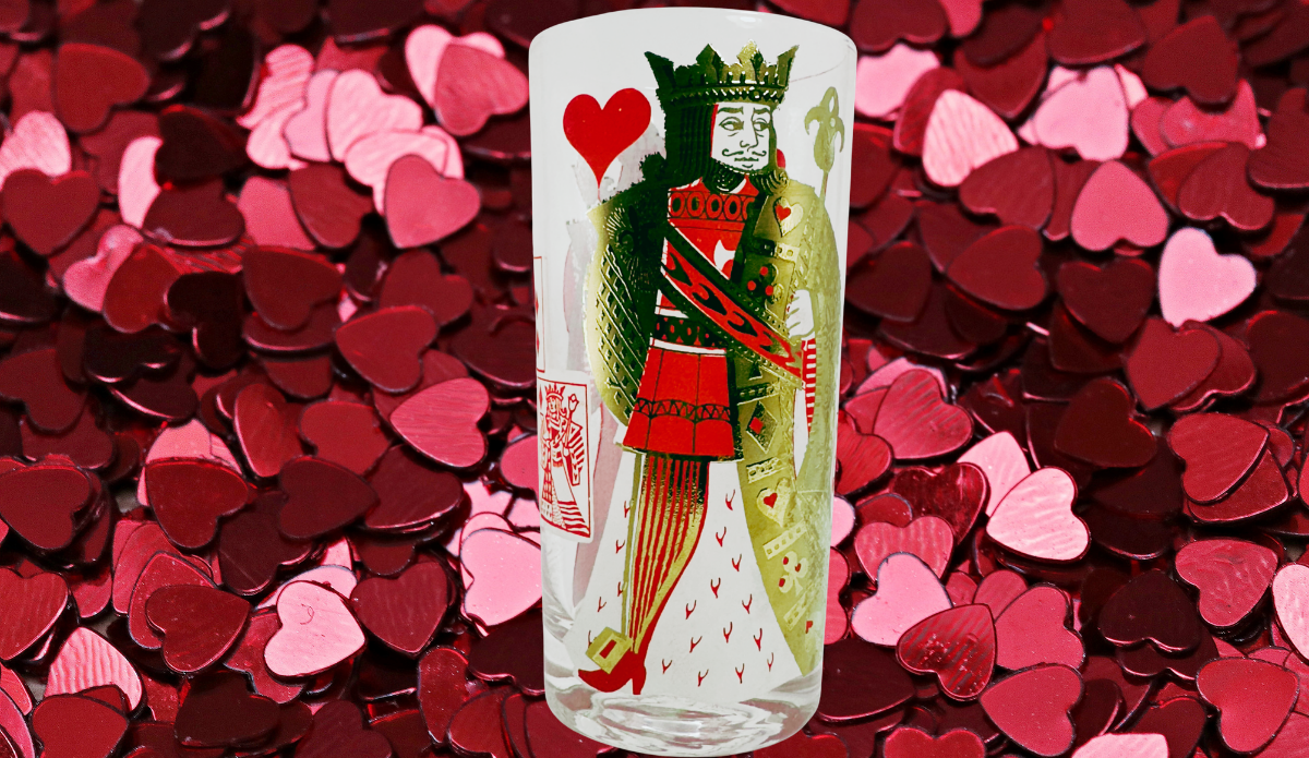 King of Hearts Playing Card Highball Glass displayed against scattered red, burgundy, and pink heart-shaped decorations.