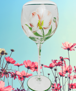 Hand Painted Peach Pink Flower Balloon Wine Glass displayed among pink and white cosmos flowers beneath a bright blue sky.