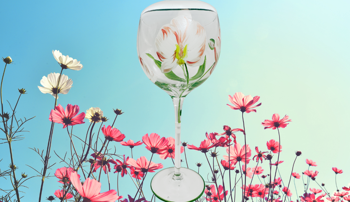 Hand Painted Peach Pink Flower Balloon Wine Glass displayed among pink and white cosmos flowers beneath a bright blue sky.