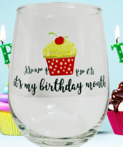 It's My Birthday Month Stemless Wine Glass displayed with colorful cupcakes, birthday candles, and a light blue party background.