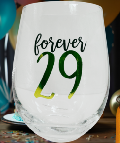 orever 29 Stemless Wine Glass displayed at a birthday party with colorful balloons and a smiling woman in a bright yellow top.