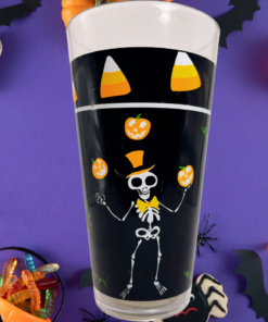 Juggling Skeleton Halloween Acrylic Tumbler surrounded by pumpkins, bats, spiders, candy, and spooky treats on purple background