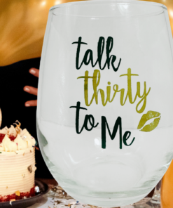 Talk Thirty To Me Stemless Wine Glass displayed beside a 30th birthday cake, gold balloons, and festive party decorations.