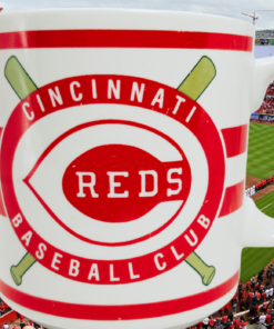 Cincinnati Reds Baseball Club Mug displayed against a Cincinnati baseball stadium filled with red-clad fans and the baseball field.
