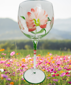 Hand Painted White Pink Flower Balloon Wine Glass displayed in a colorful flower meadow with pink wildflowers, green hills and distant mountains.