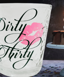 Dirty Thirty Whiskey Glass displayed beside a chocolate 30th birthday cake topped with sparkling silver 30 candles.