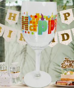Happy Birthday Colorful Lettering Wine Glass displayed at a decorated party table with birthday banner, pastel balloons, cake, and treats.