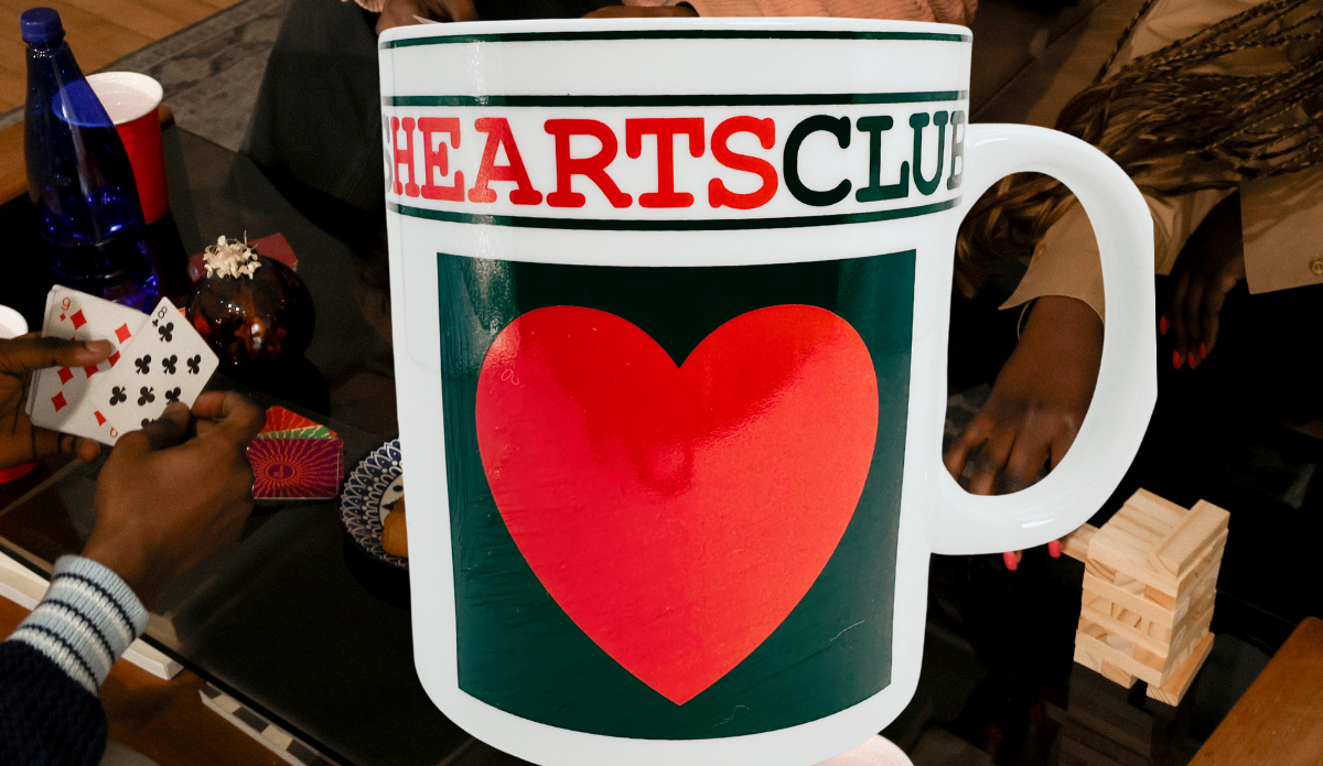 Hearts Playing Cards Coffee Mug displayed at a game-night table with playing cards, a wooden stacking game, and people gathered around.