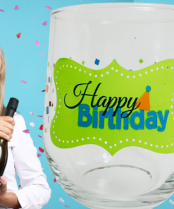 Happy Birthday Confetti Stemless Wine Glass displayed beside a smiling woman wearing a pink party hat and holding a dark bottle against a blue birthday background.