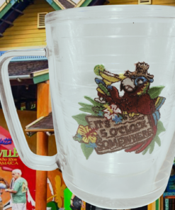 Tervis Margaritaville Red Parrot Mug displayed against Jimmy Buffett's Margaritaville in Ocho Rios, Jamaica, with colorful tropical buildings and signage.