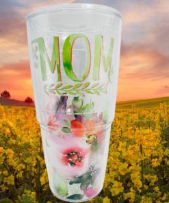 Tervis Mom Watercolor Floral Tumbler displayed in a field of golden-yellow flowers beneath a pink and orange sunset sky.