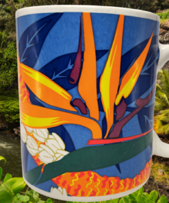 Hilo Hattie Bird of Paradise Hawaiian Coffee Mug lifestyle scene featuring tropical flowers against a Hawaiian waterfall and palm trees.